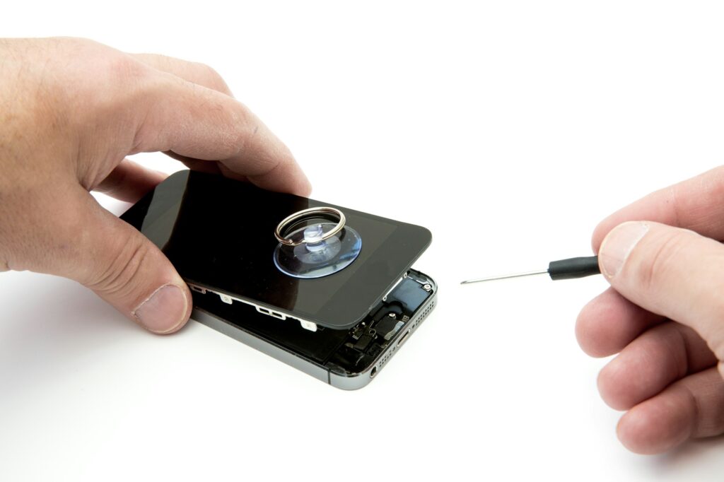 A pair of hands repairing a broken and damaged mobile phone or cell phone screen on white background